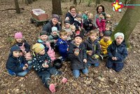 Kinder, Erzieherinnen und Andrea Sassenberg vom Grünen Klassenzimmer sitzen auf dem Waldboden.